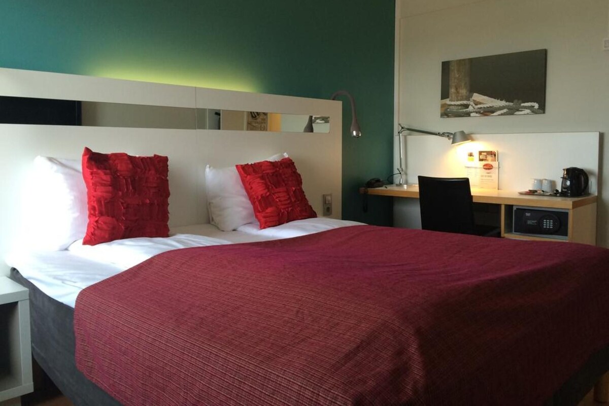 A hotel room with a bed, a desk, and a chair.