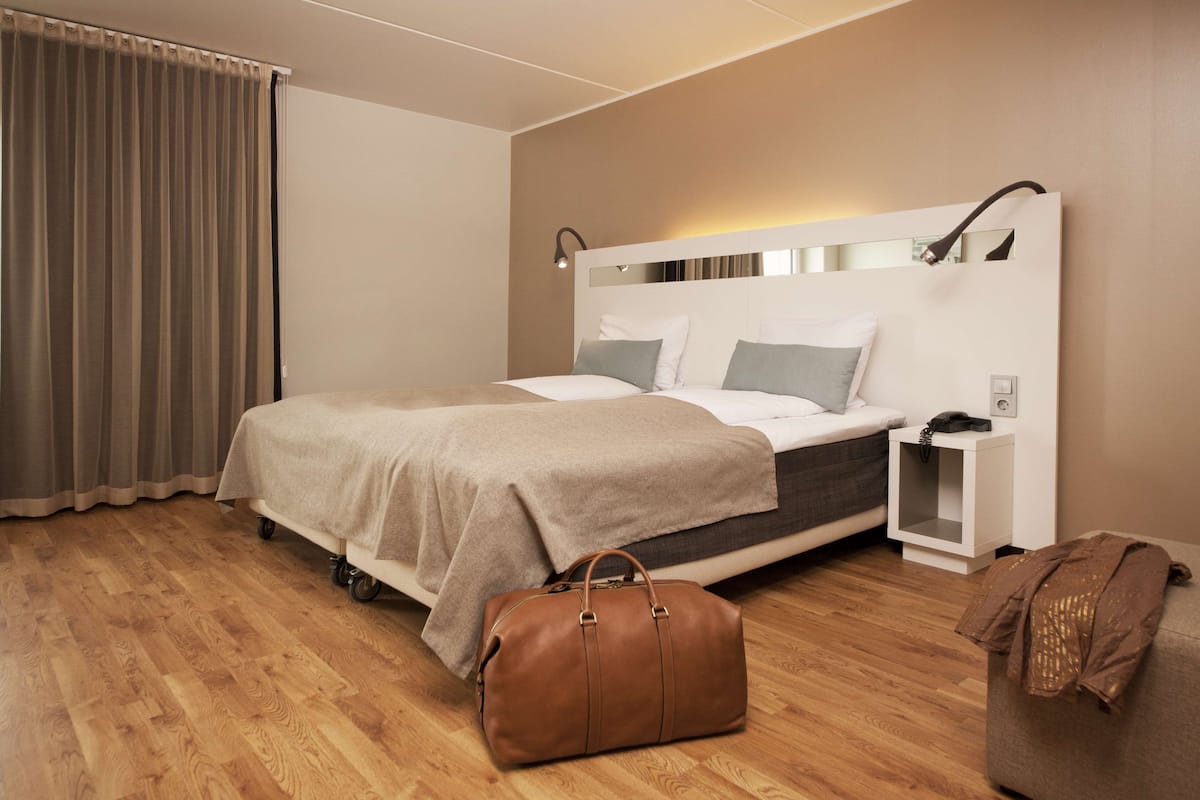 A modern hotel room with a bed, bedside table, and a brown leather bag on the floor.