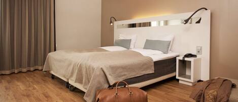 A modern hotel room with a bed, bedside table, and a brown leather bag on the floor.