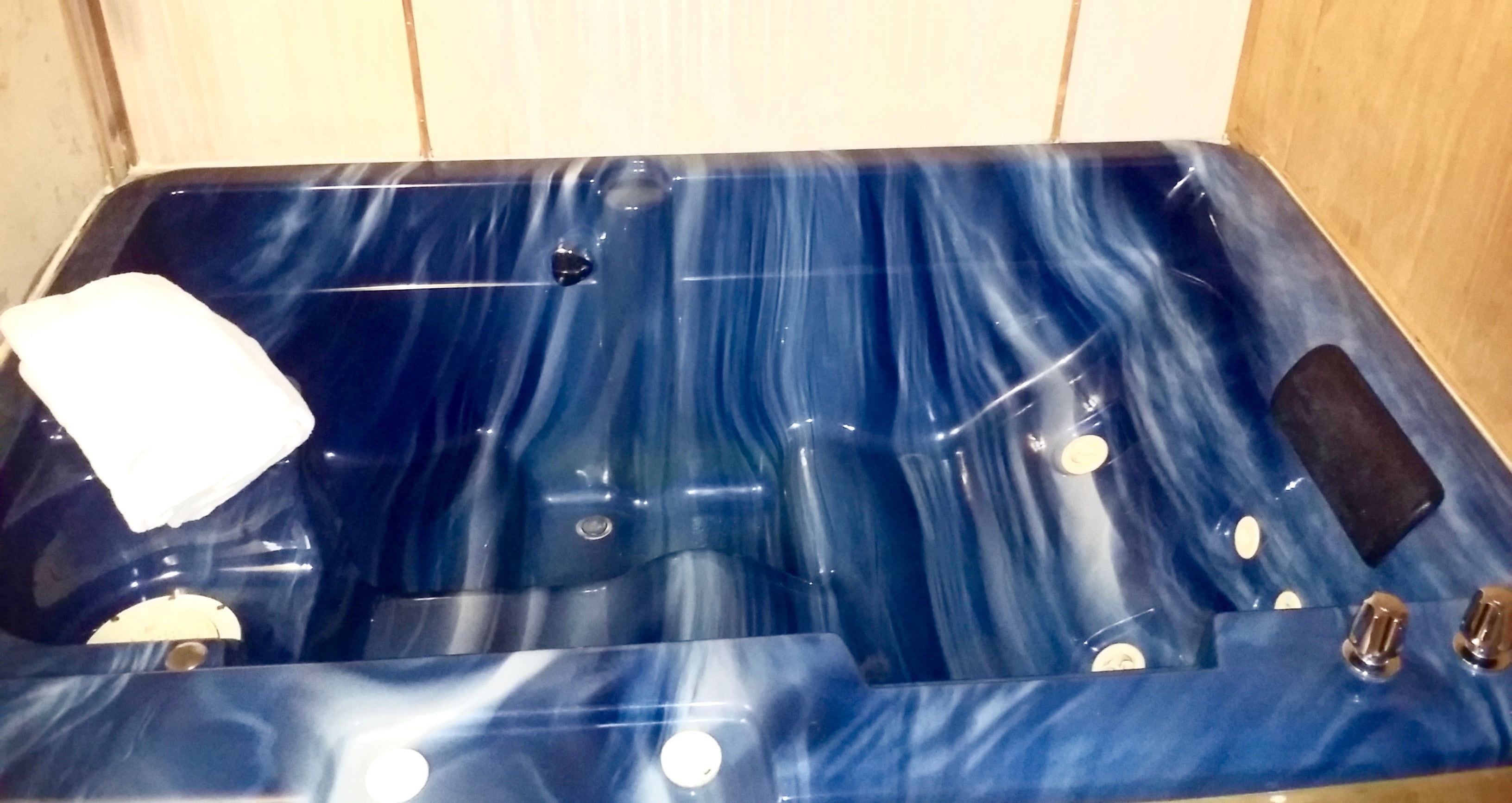 A blue jacuzzi with a white towel, a control panel, and a small black object on the side.