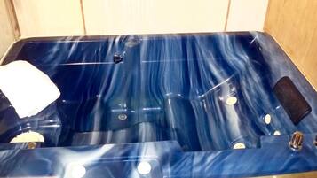 A blue jacuzzi with a white towel, a control panel, and a small black object on the side.