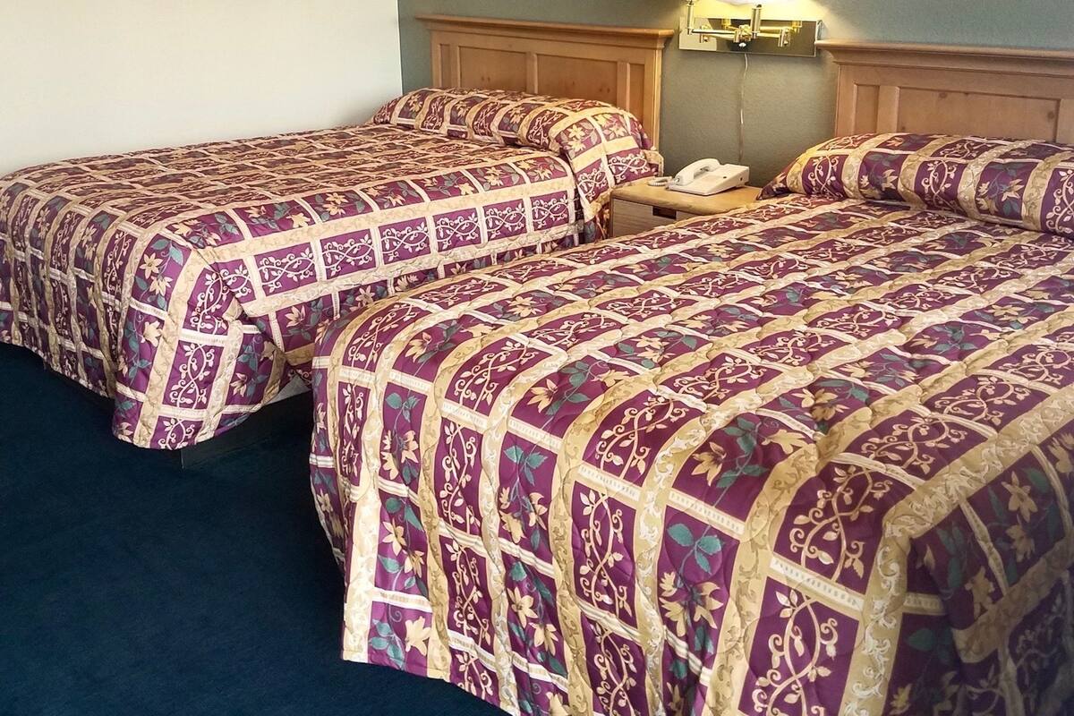 A hotel room with two beds, each with a patterned bedspread, a nightstand with a lamp, and a framed painting on the wall.