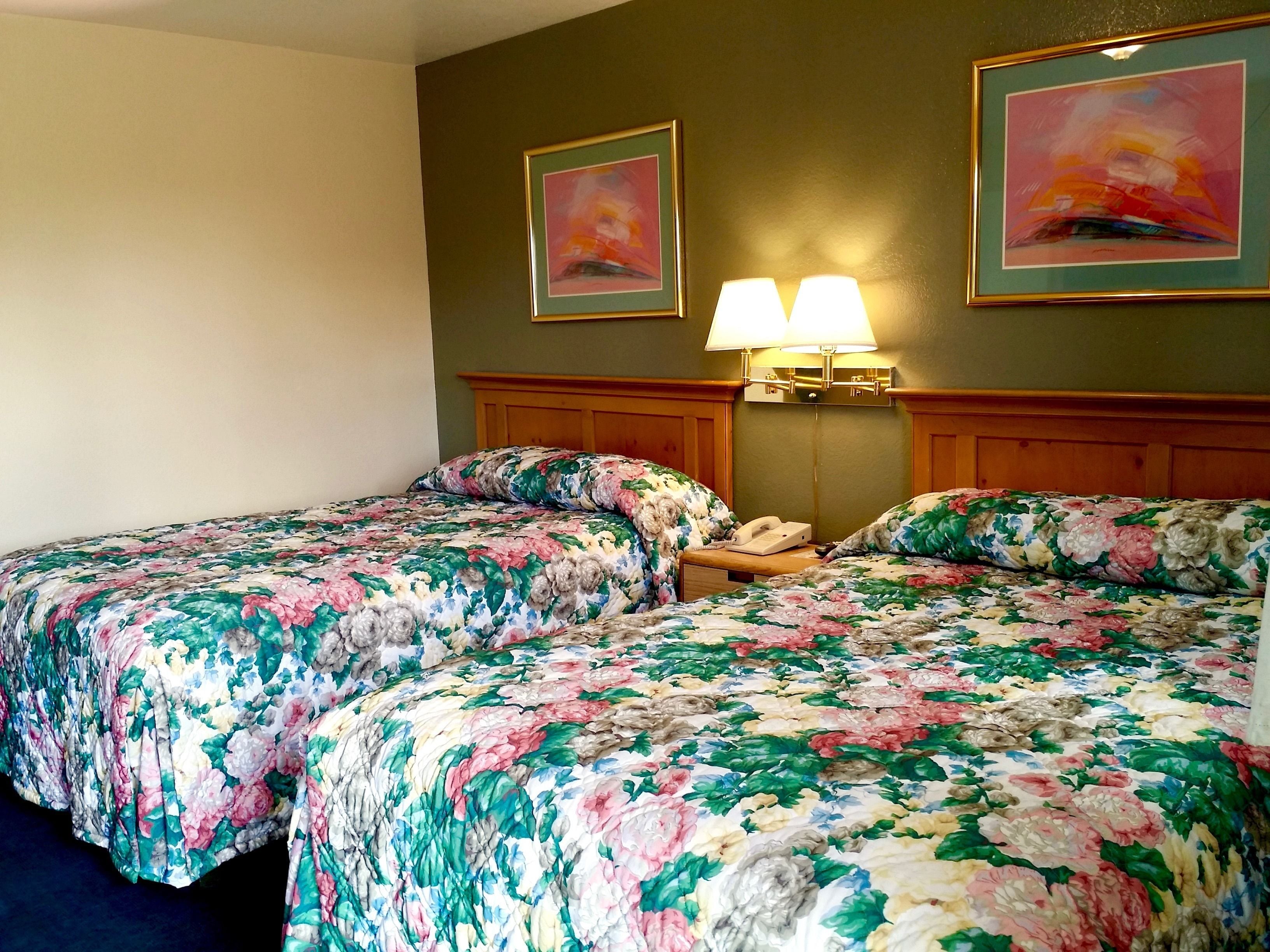 Habitación de hotel con dos camas, ropa de cama floral, una mesita de noche con lámpara y dos cuadros en la pared.