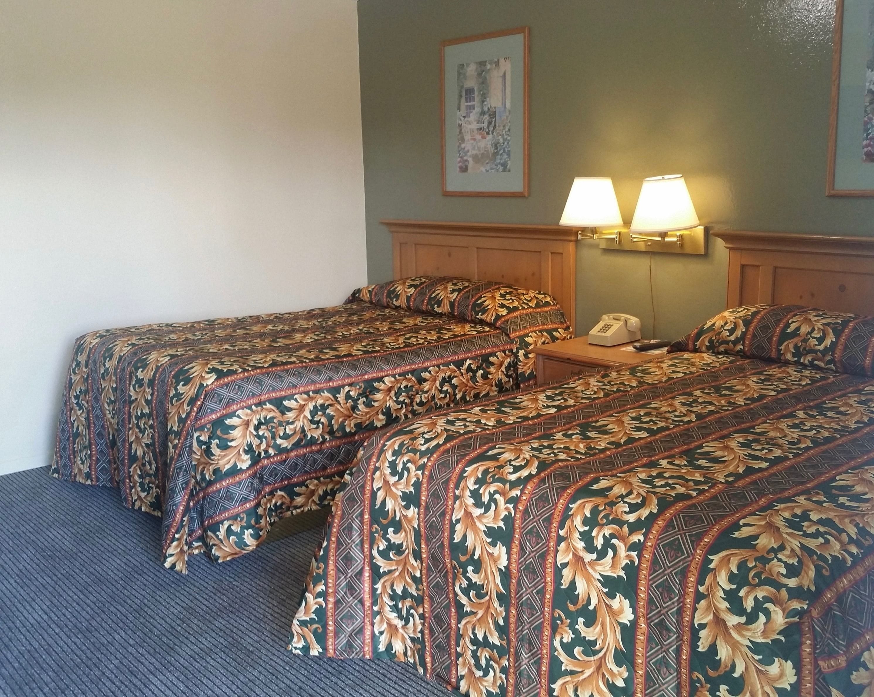A hotel room with two beds, a nightstand with a telephone, and wall-mounted lamps.