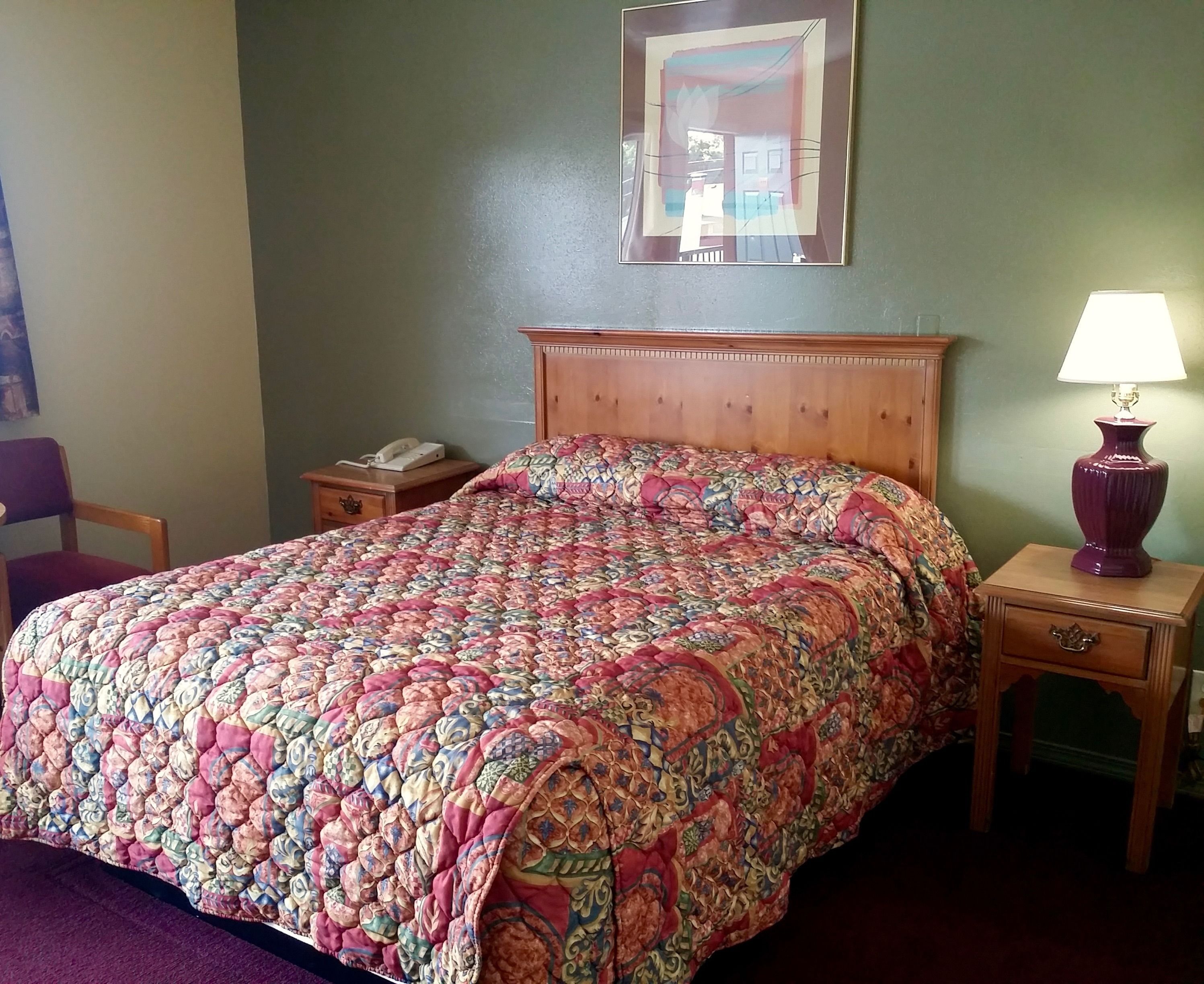 A neatly made bed with a patterned bedspread, a wooden headboard, a bedside lamp, and a nightstand with a telephone.