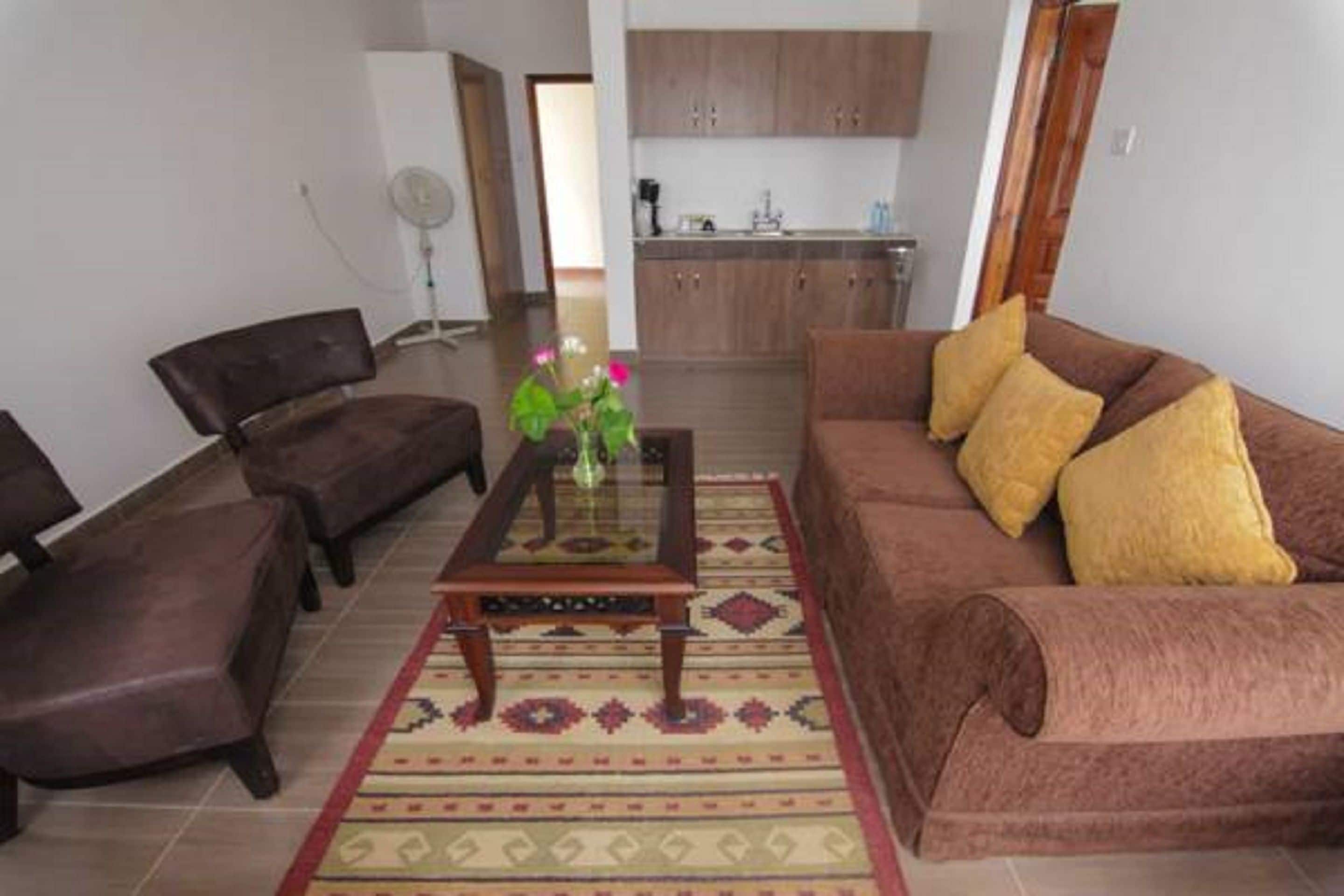 A living room with a brown sofa, two armchairs, a glass coffee table, and a patterned rug.