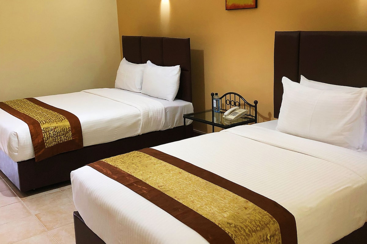 Deux lits simples avec des têtes de lit marron et du linge de lit blanc, une petite table de chevet avec un téléphone et un luminaire fixé au mur.