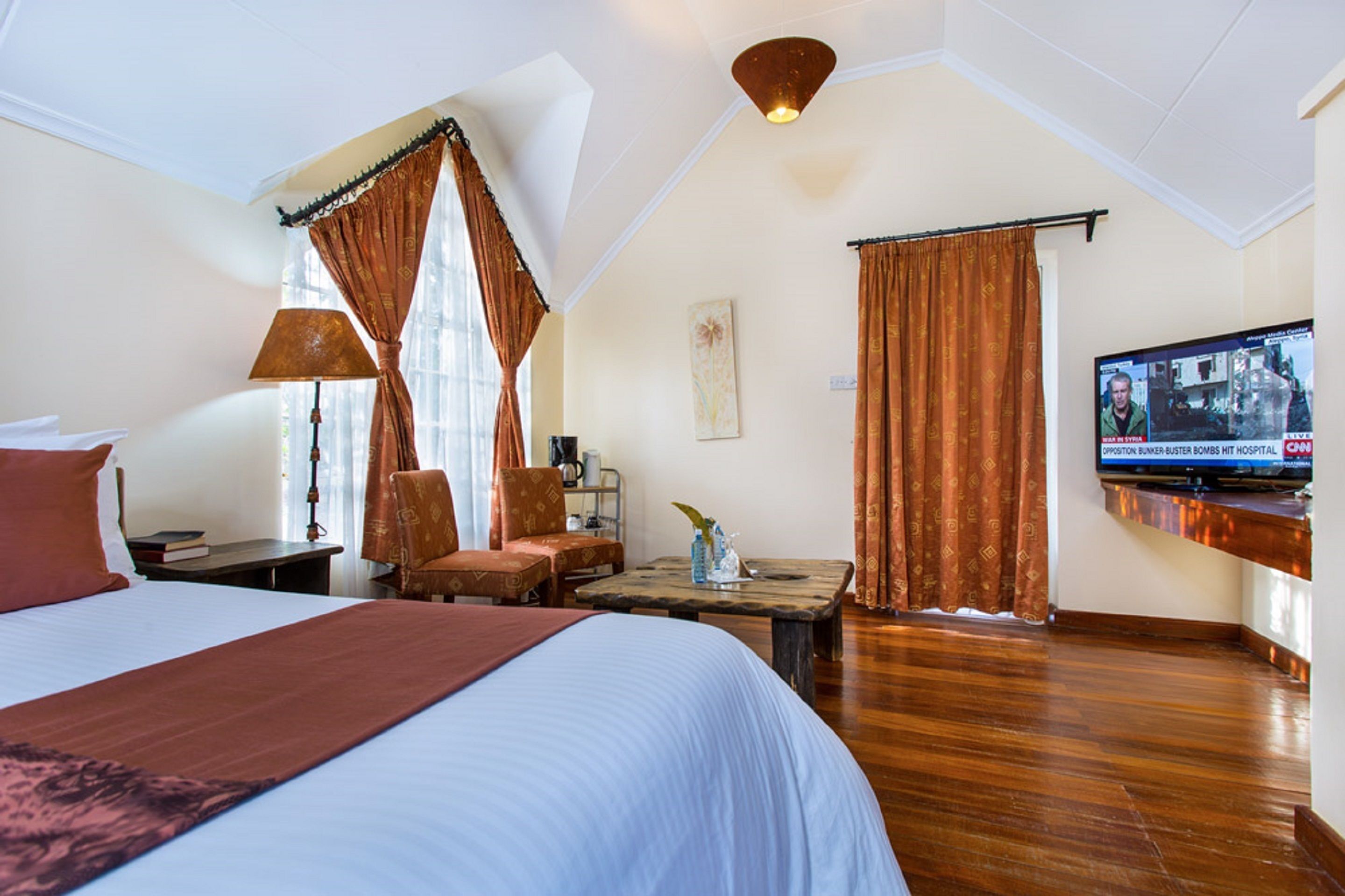 Habitación de hotel con una cama grande, dos sillas, una mesita, un televisor y cortinas.