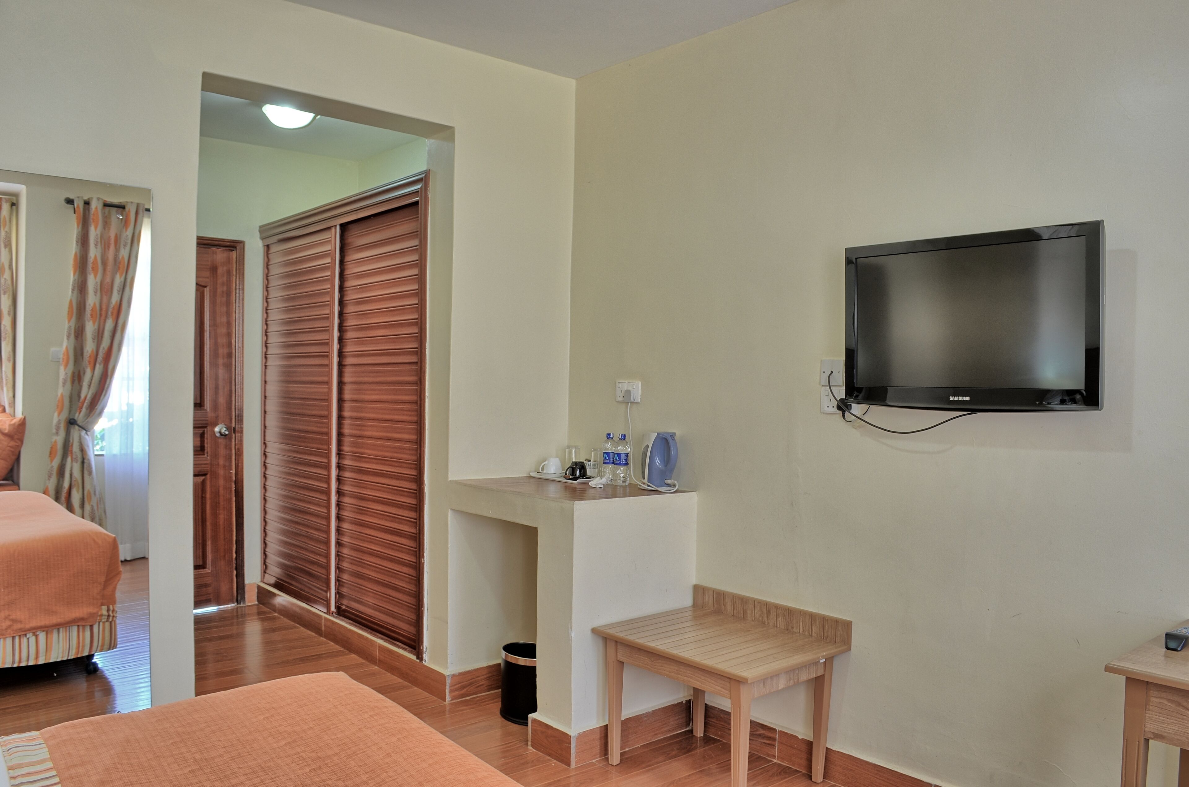 A hotel room with a bed, a TV mounted on the wall, a small wooden table, and a desk with a chair.