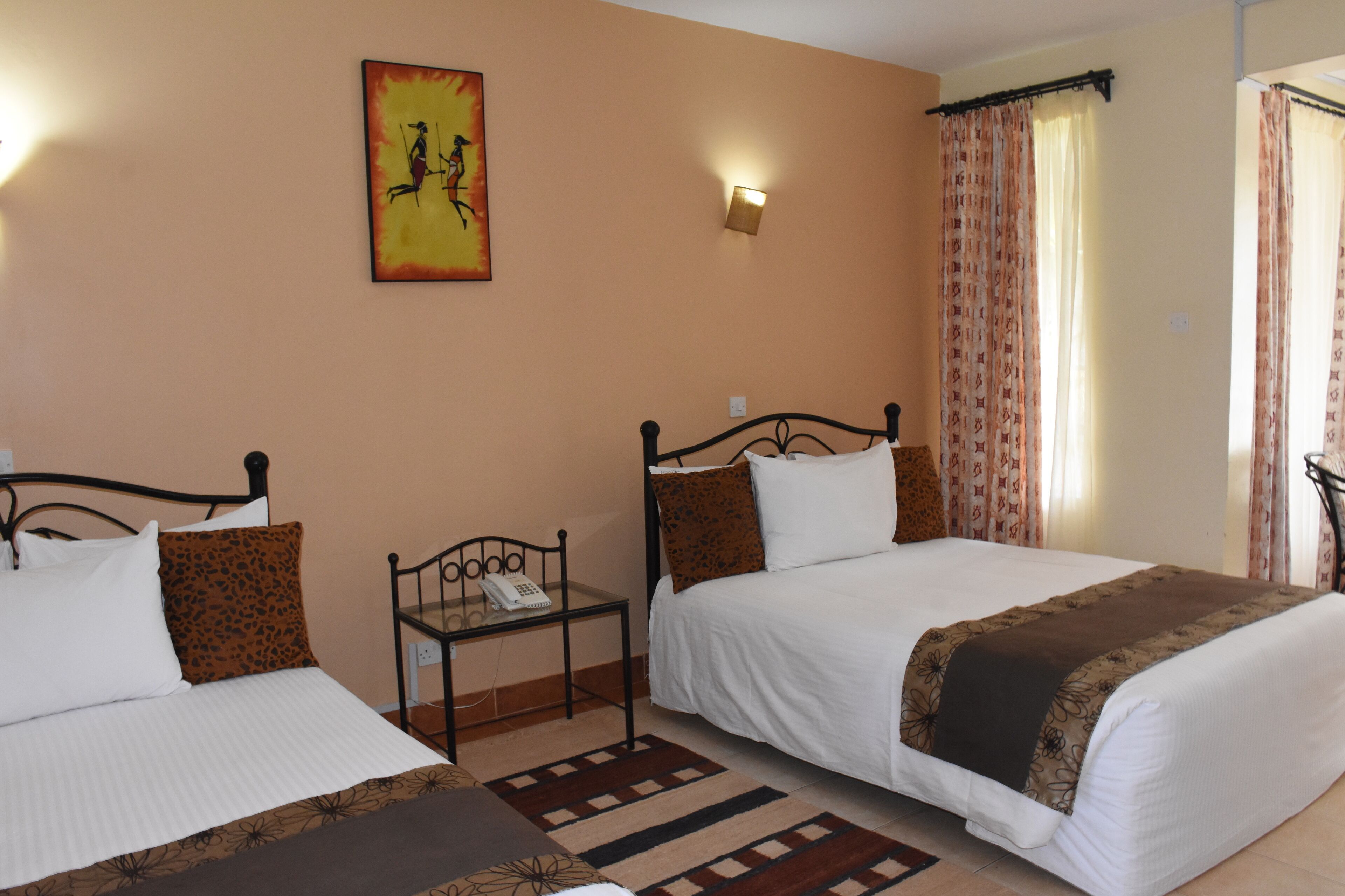 Une chambre d’hôtel avec deux lits, une petite table avec un téléphone, une lampe fixée au mur et un tableau.