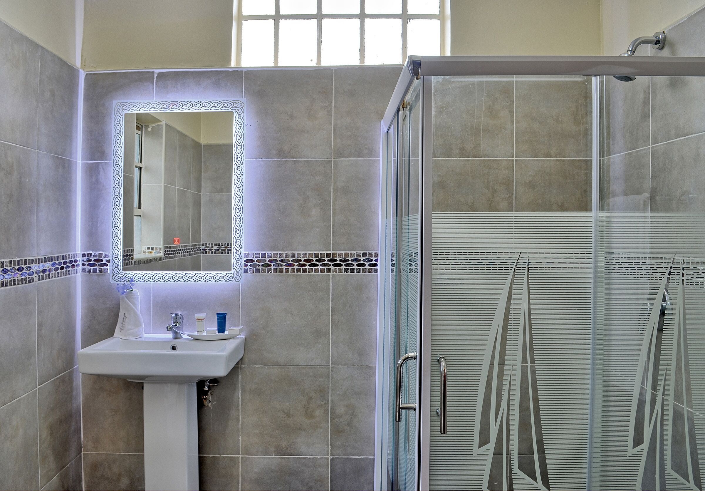 A bathroom with a glass shower enclosure, a sink with a mirror, and tiled walls.