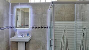 A bathroom with a glass shower enclosure, a sink with a mirror, and tiled walls.