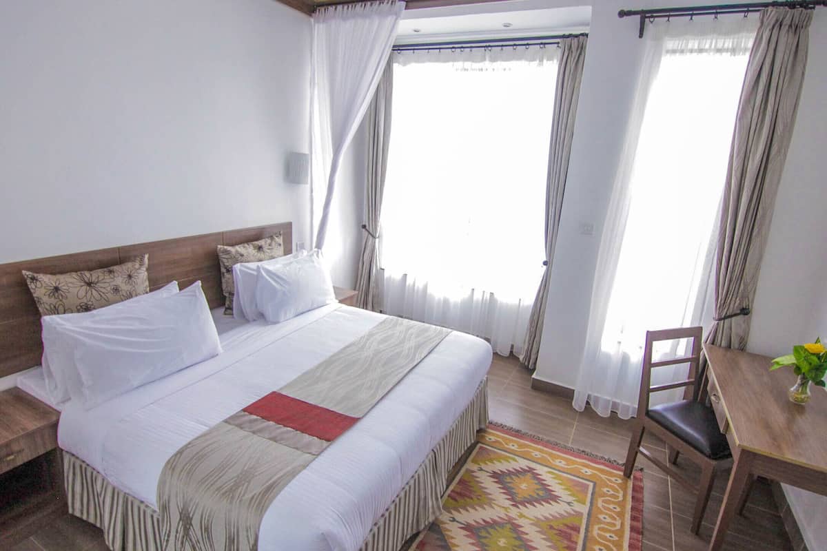 Une chambre à coucher avec un grand lit, une tête de lit en bois, un bureau avec une chaise et une fenêtre avec des rideaux.