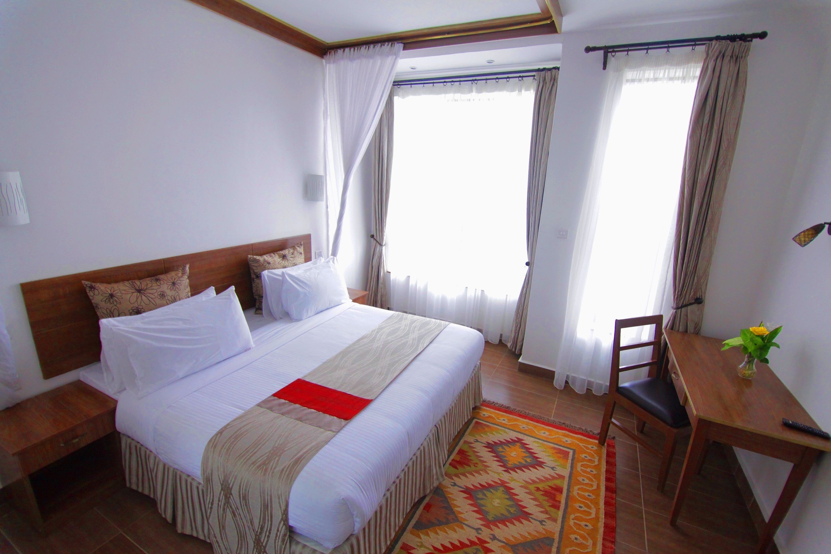 Quarto de hotel com uma cama grande, mesa de cabeceira de madeira, escrivaninha e uma cadeira.