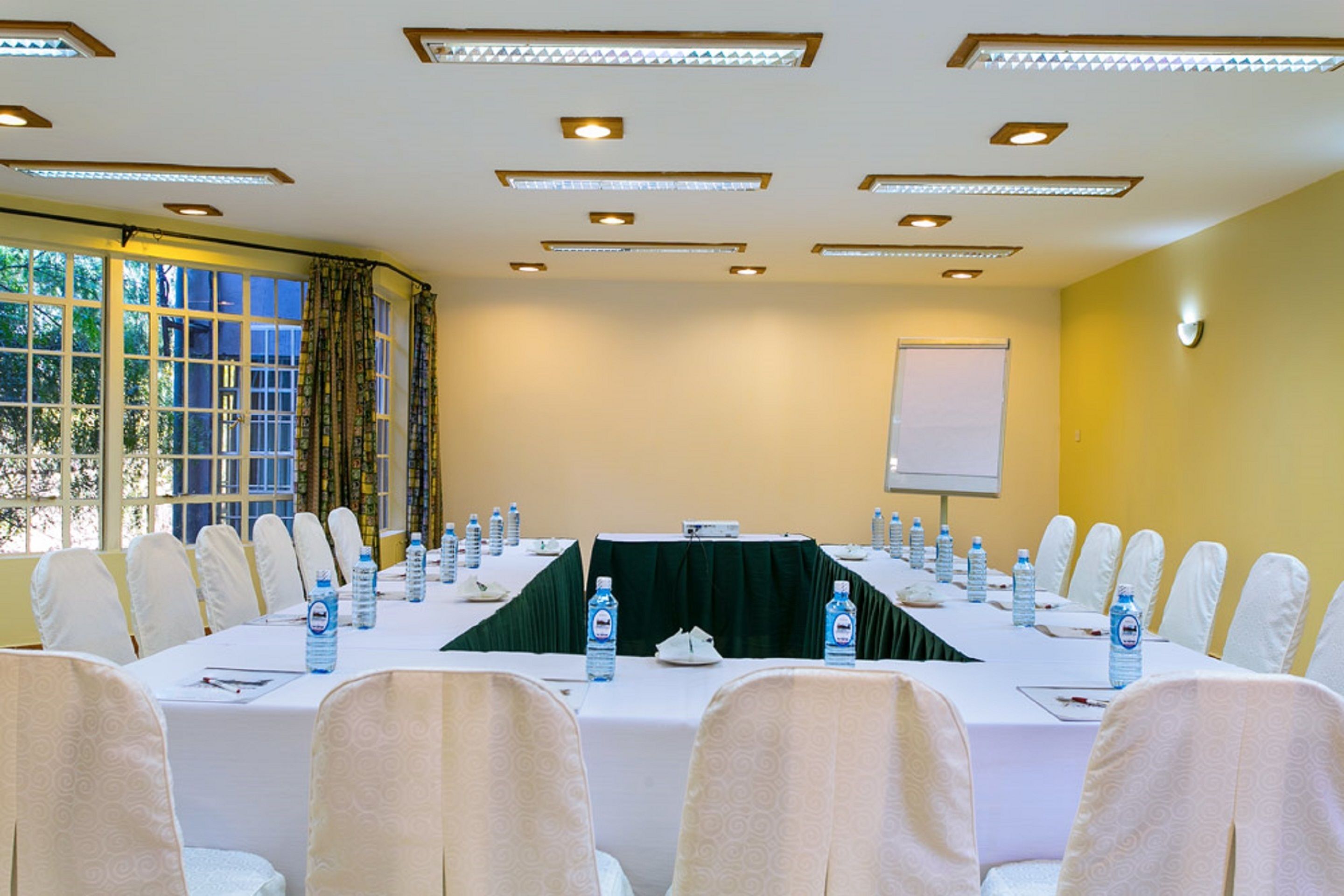 A conference room with a long table, white chairs, water bottles, and a projector screen.