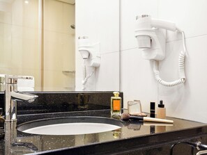 A bathroom with a black granite sink, a mirror, a hairdryer mounted on the wall, and toiletries on the counter. - ibis Dubai Al Rigga (Dubai)