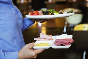 A person holding a tray with various food items including sliced meats and vegetables.