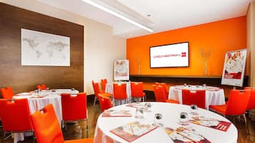 A conference room with round tables, orange chairs, white tablecloths, a world map on the wall, and a screen displaying 'Lively Meetings by ibis'.