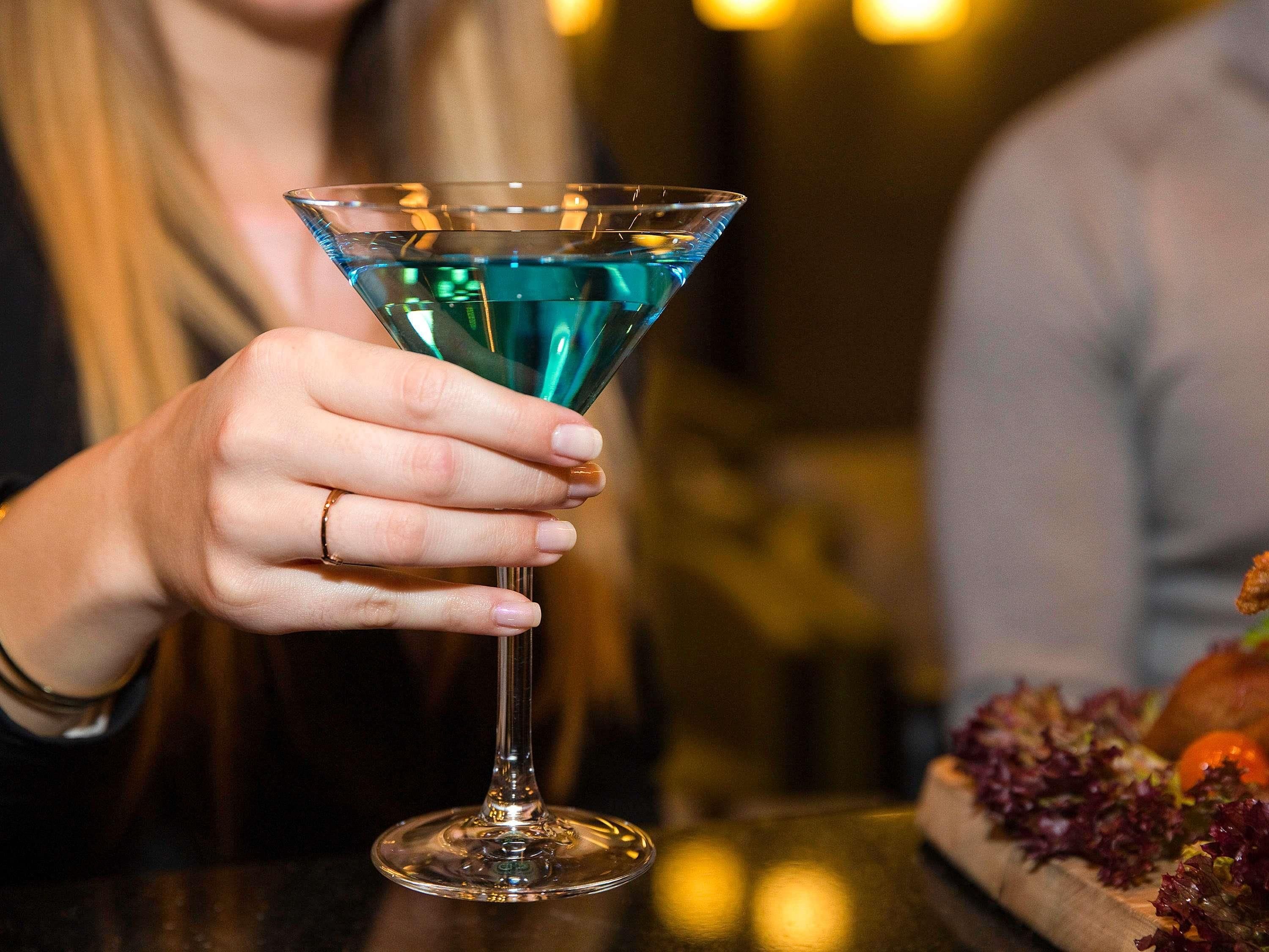 A person holding a martini glass with a blue liquid.