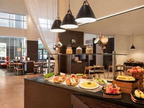 En modern hotellobby med ett område för buffé, sittplatser och ett stort fönster som släpper in naturligt ljus.