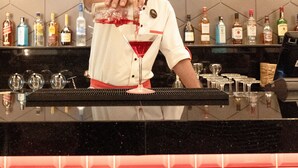 A bartender pouring a drink at a bar with a hexagonal patterned wall and various bottles in the background. - ibis Dubai Al Rigga (Dubai)