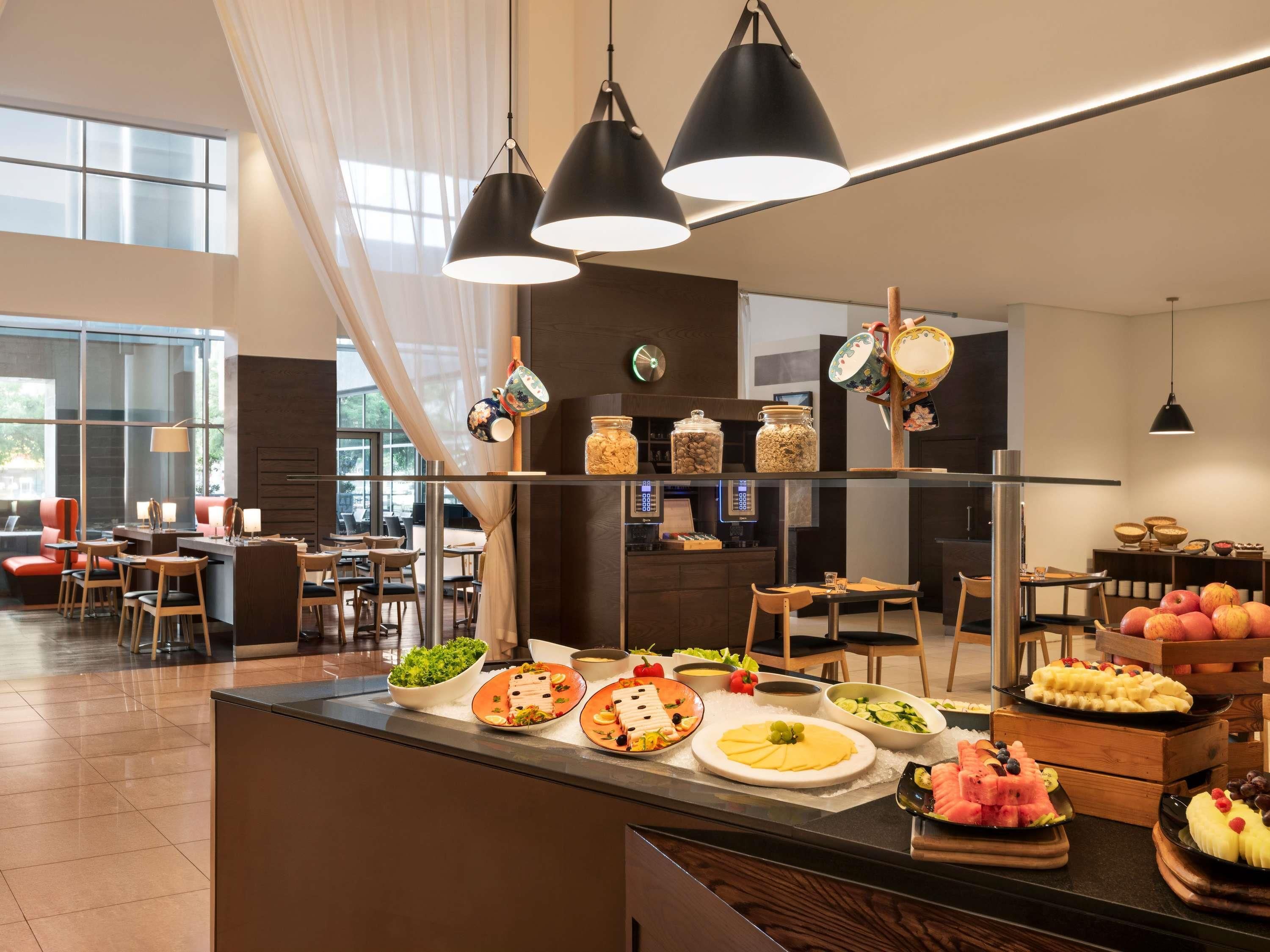 A modern hotel lobby with a buffet area, seating arrangements, and a large window providing natural light.