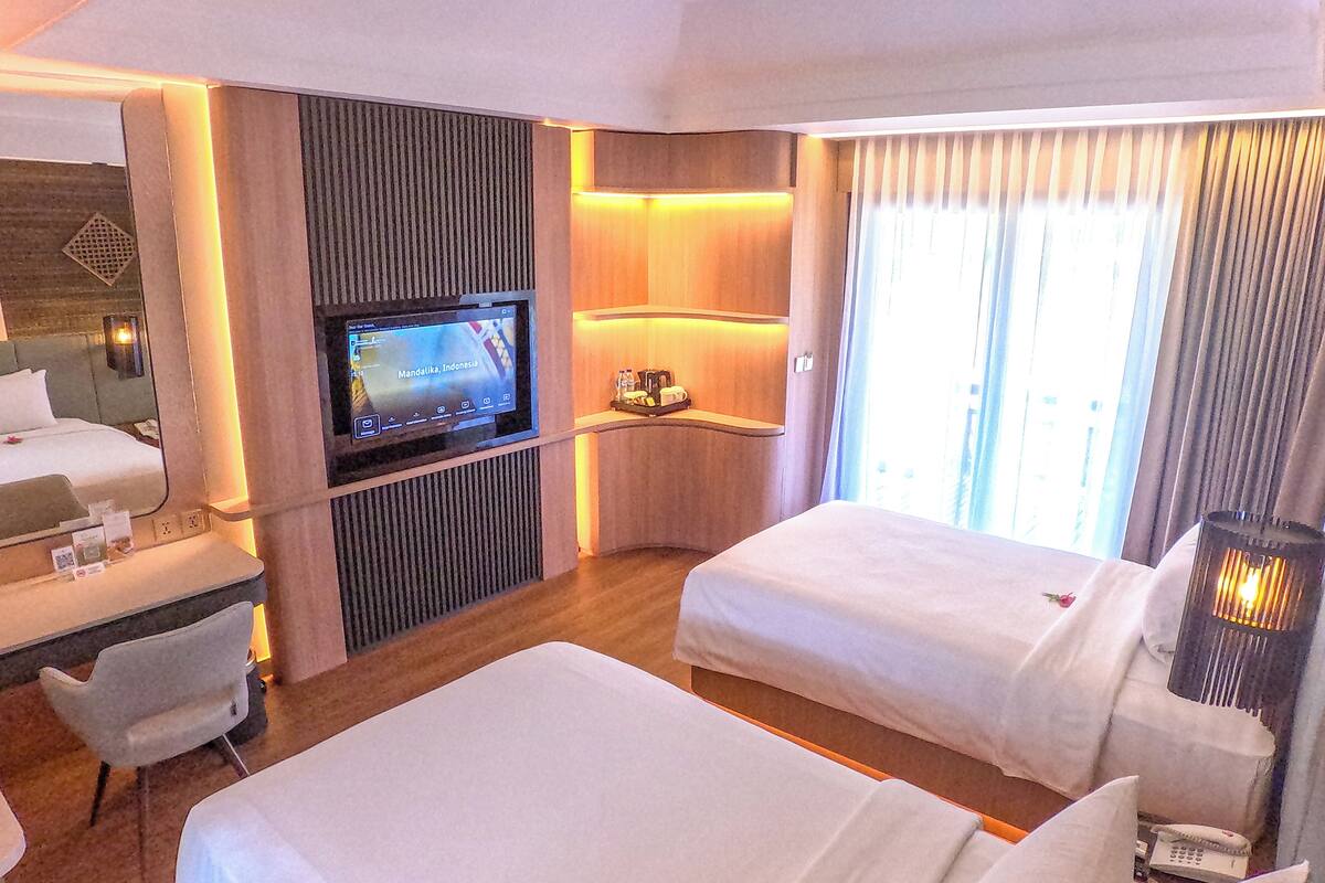 A hotel room with a TV, two beds, a desk, and a chair.