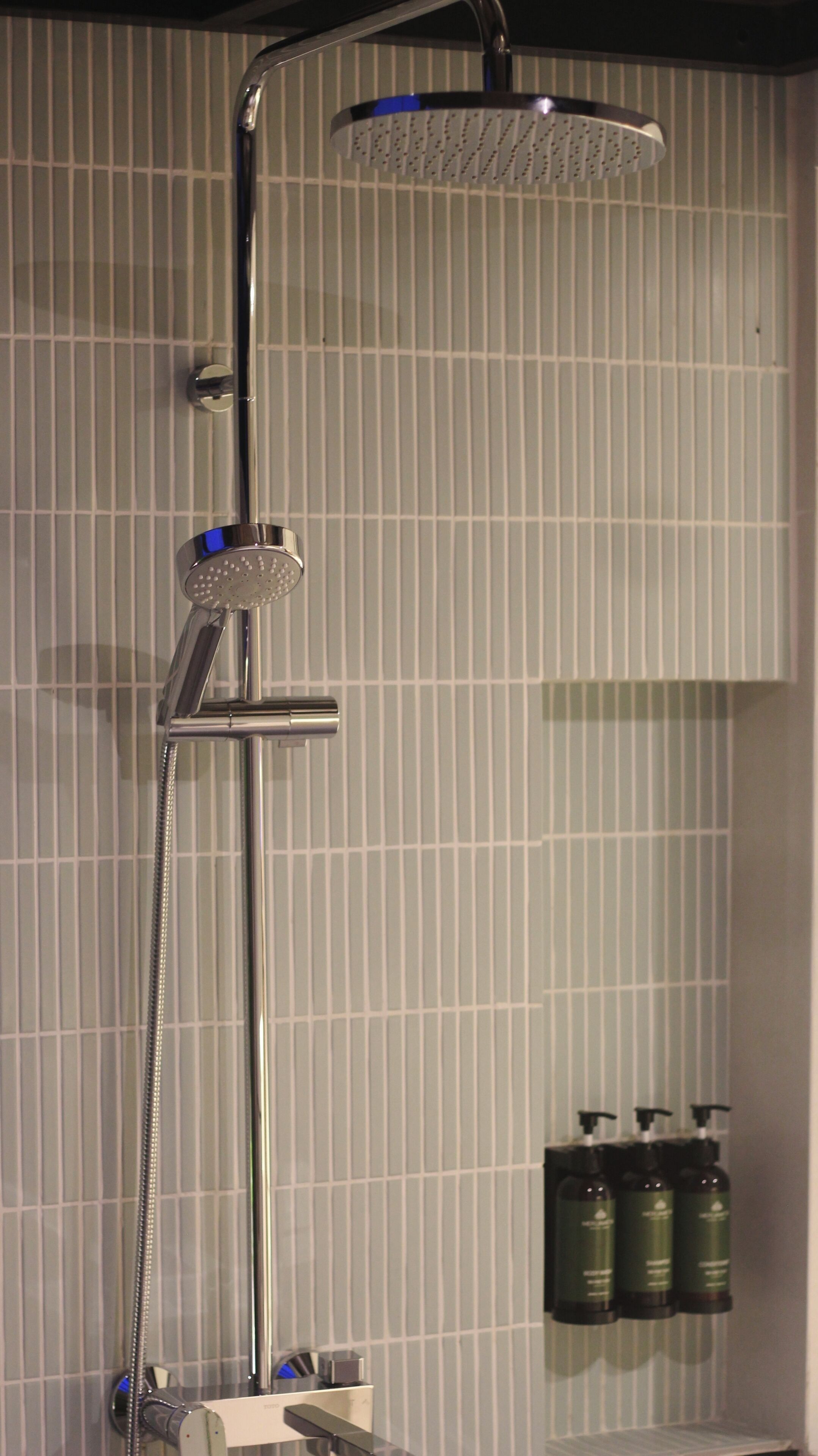 A shower with a handheld rainhead, a handheld showerhead, and a wall-mounted control panel.