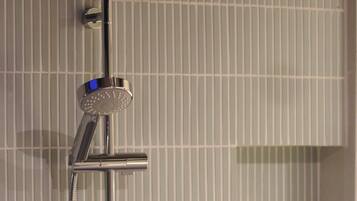 A shower with a handheld rainhead, a handheld showerhead, and a wall-mounted control panel.