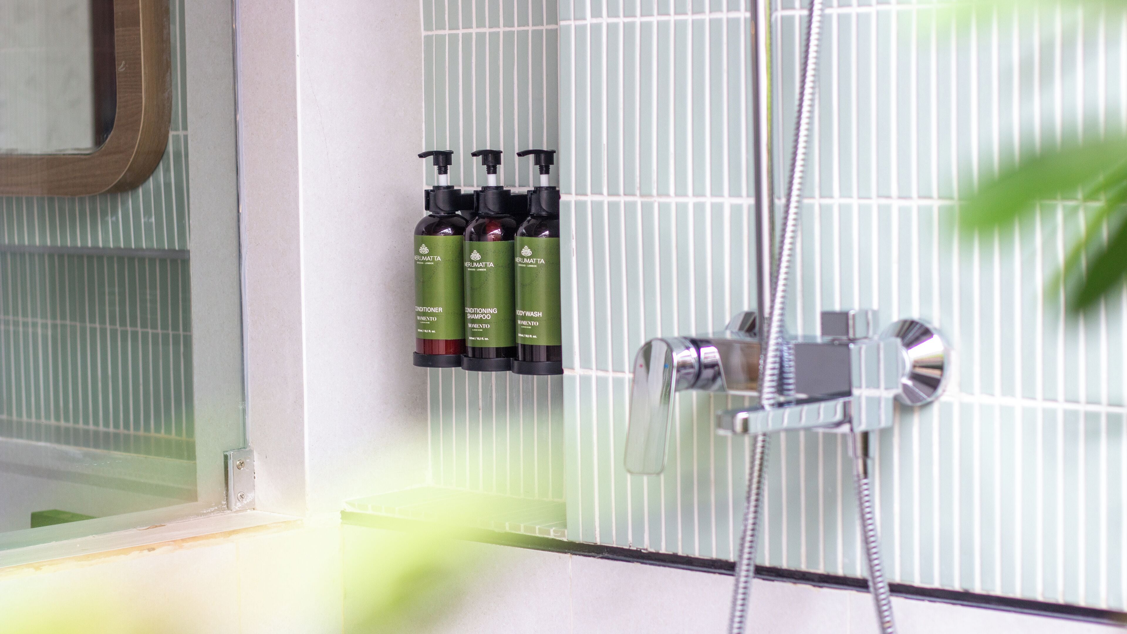 A bathroom with a shower, a mirror, and three bottles of shampoo on the wall.
