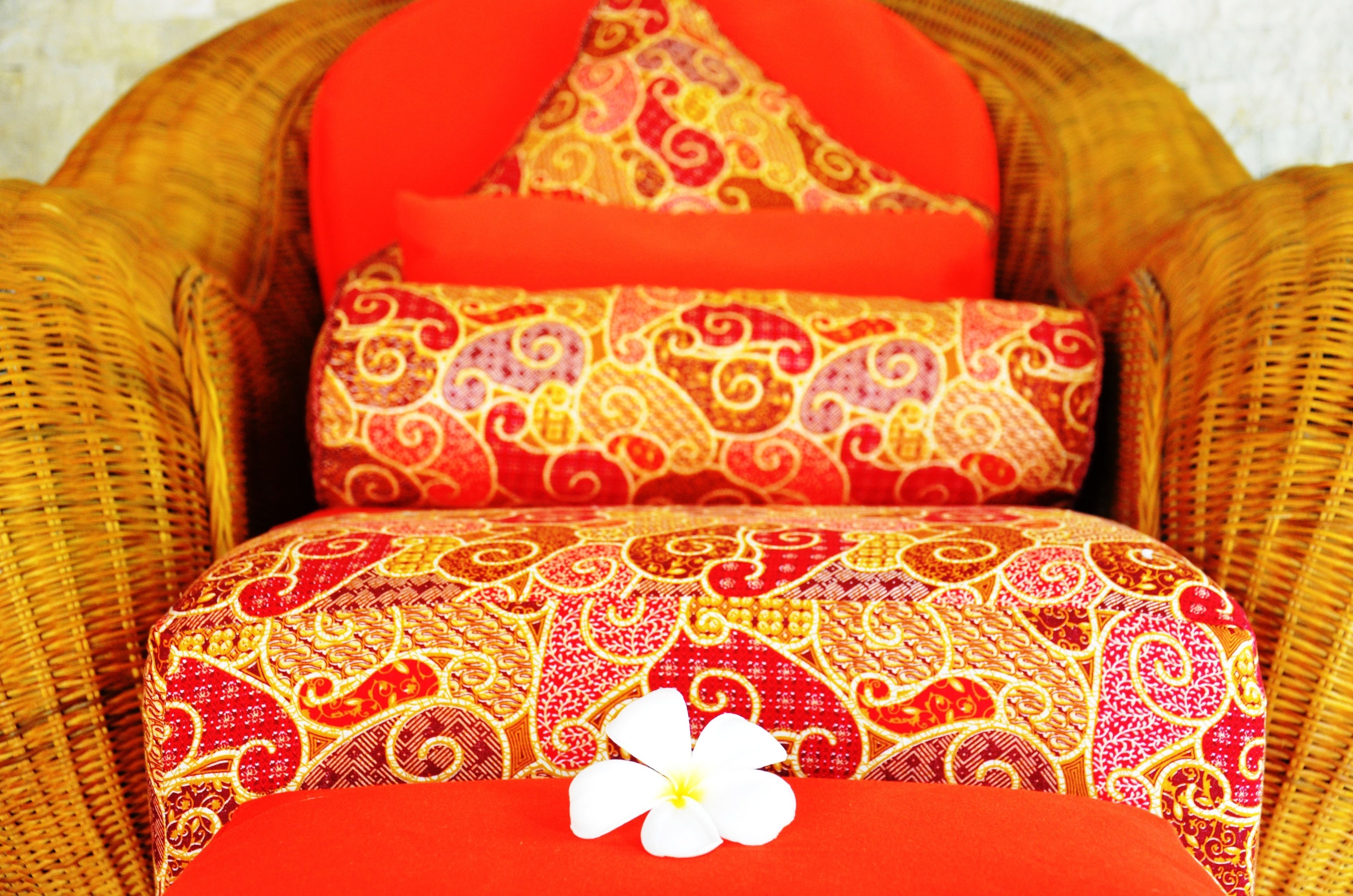 A wicker chair with red and gold patterned cushions.
