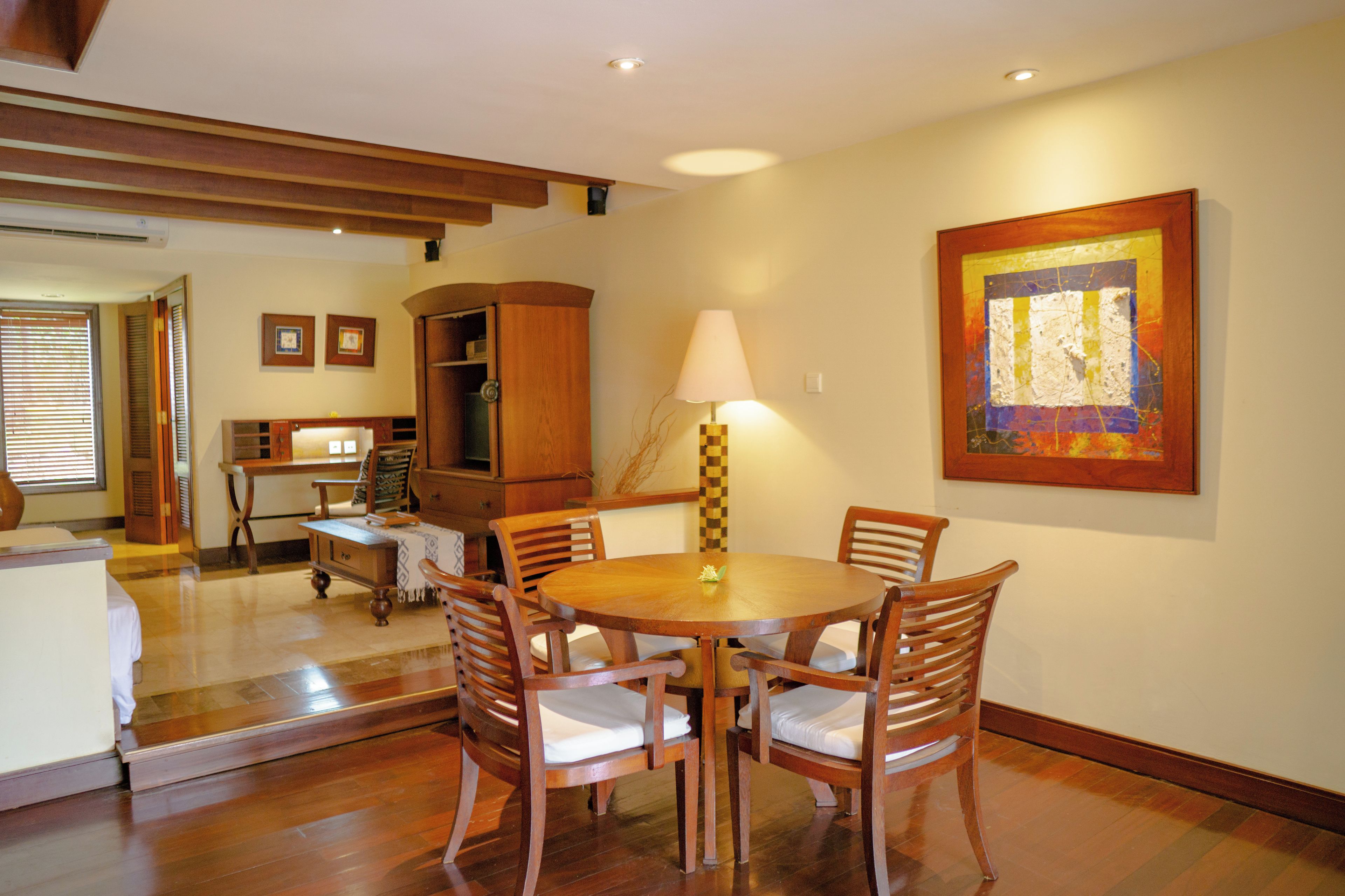 A dining area with a wooden table and chairs, a lamp, and a painting on the wall.
