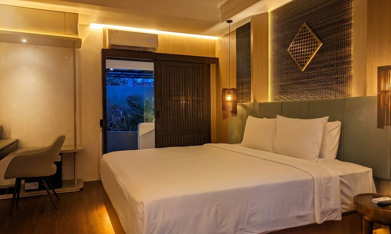 A hotel room with a bed, desk, chair, and a view of the outdoors.