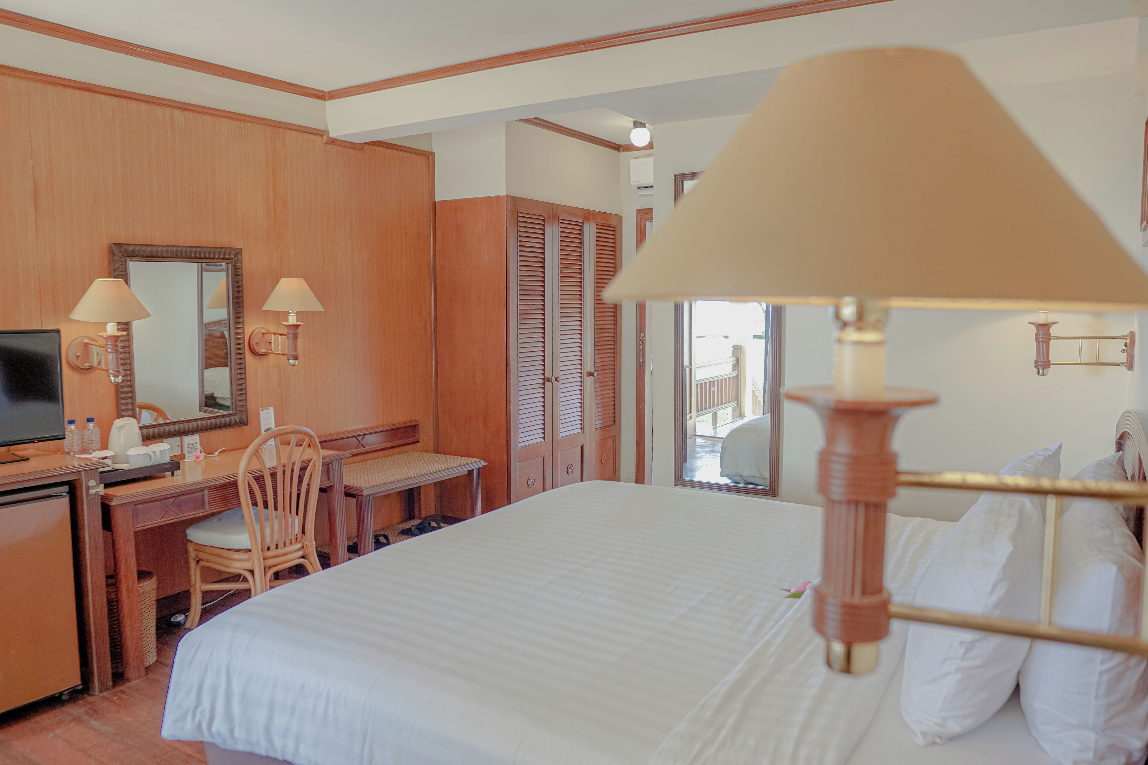 A hotel room with a bed, desk, chair, television, and wooden wardrobe.
