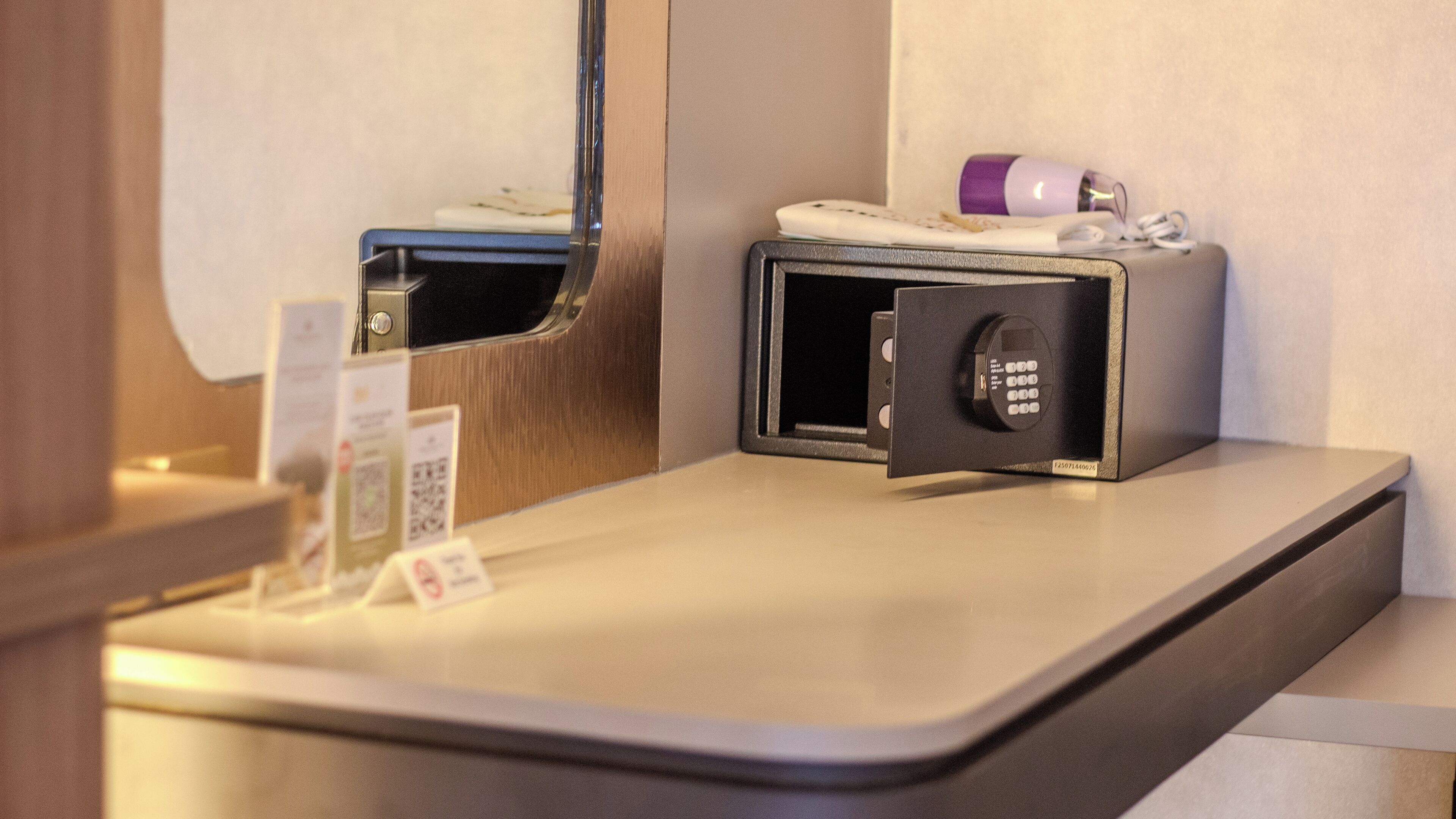 Un minibár de hotel con una caja fuerte, una botella de loción y una pequeña bandeja con un control remoto.