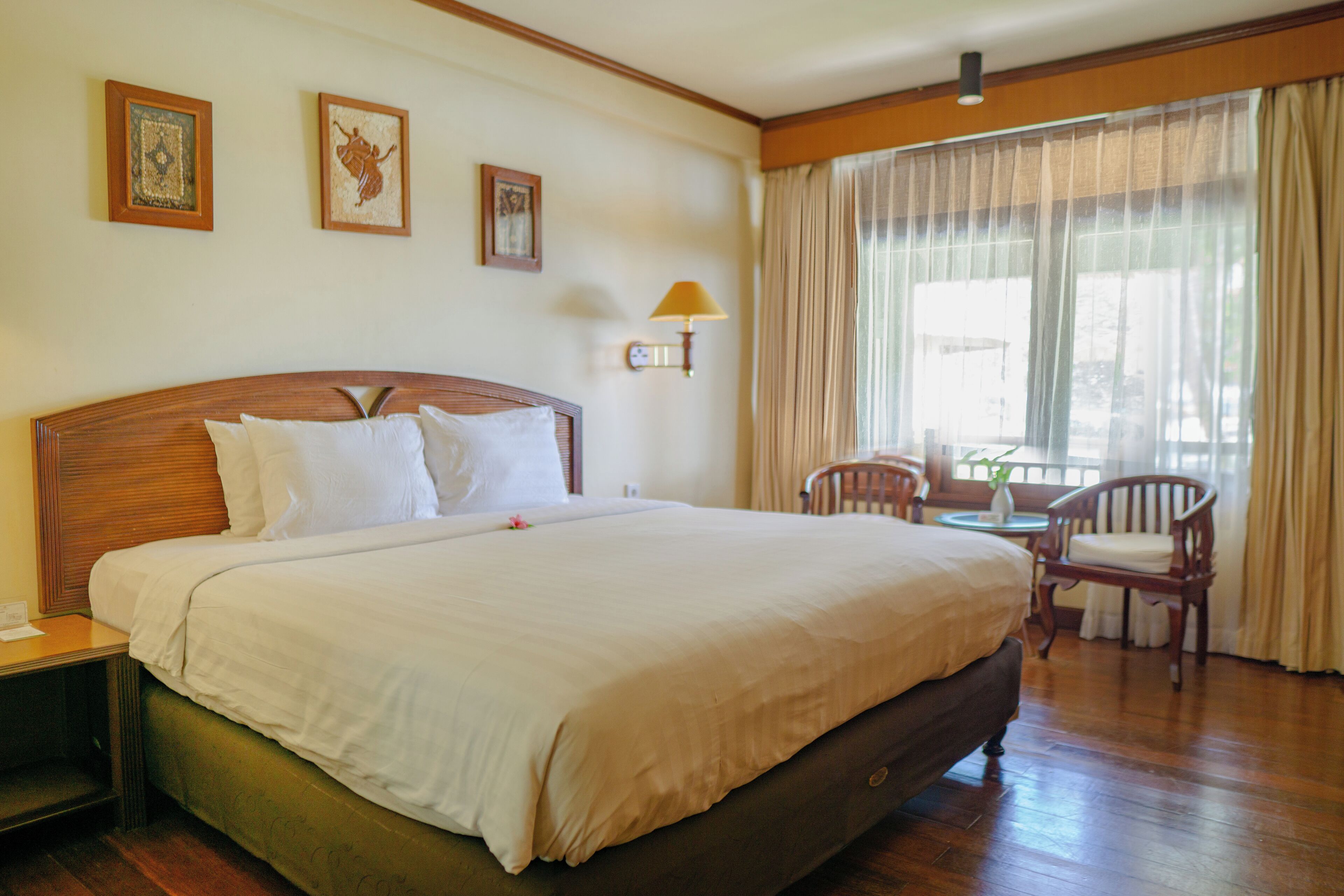 A hotel room with a large bed, a nightstand, a chair, a small table, and a window with curtains.