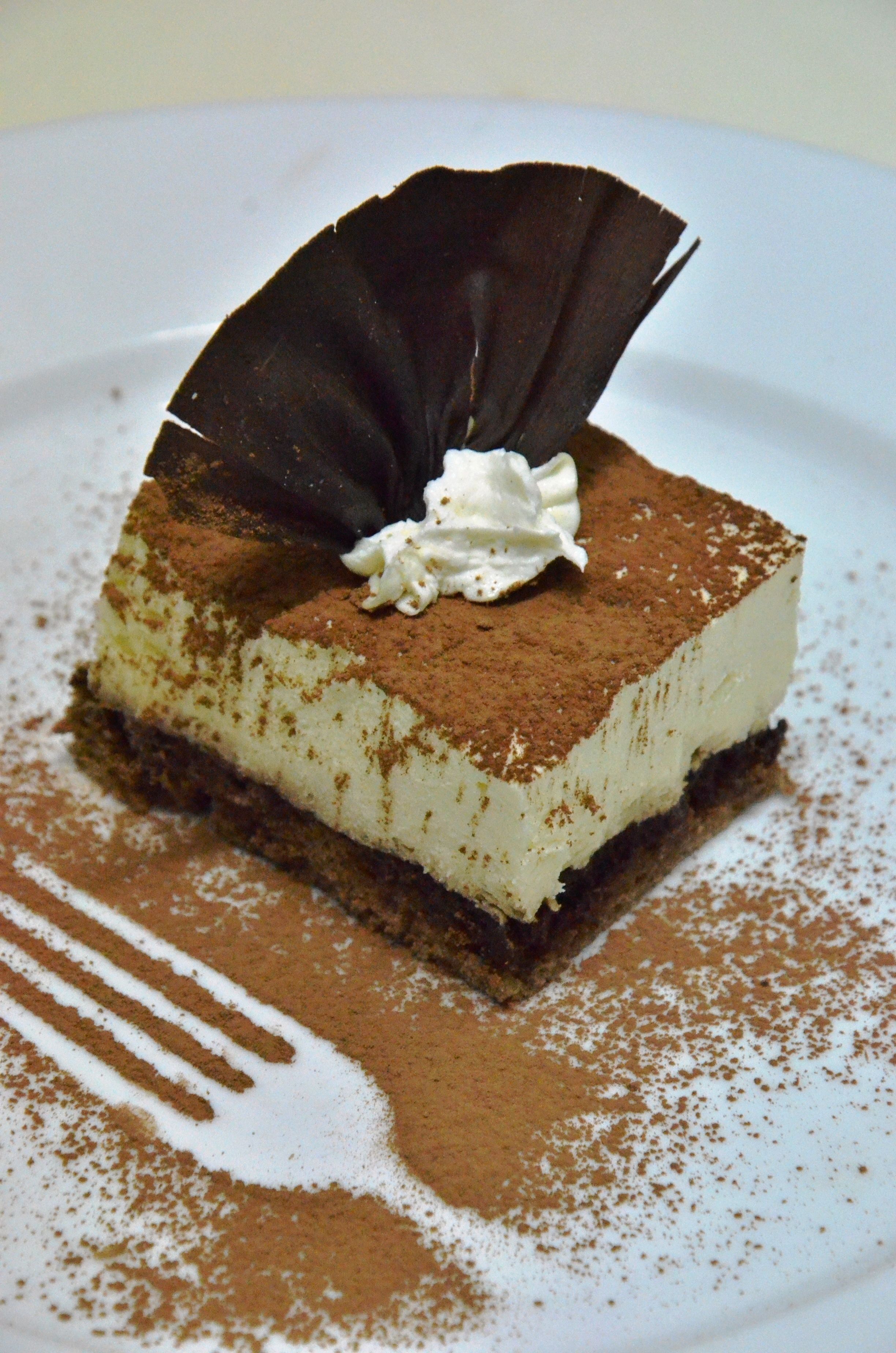Una porción de tiramisú sobre un plato blanco con un toque de cacao en polvo.