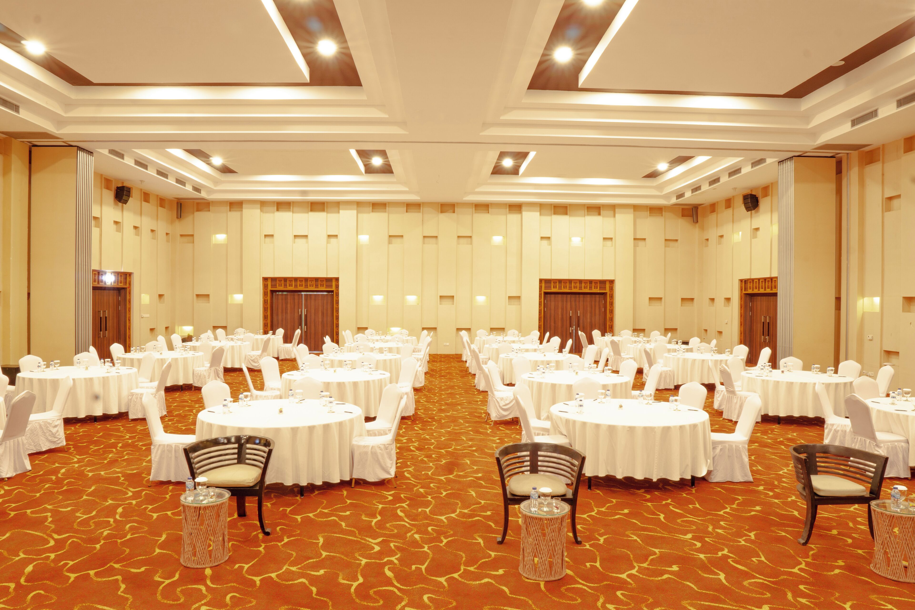 A large conference room with multiple round tables, white chairs, and a carpeted floor.