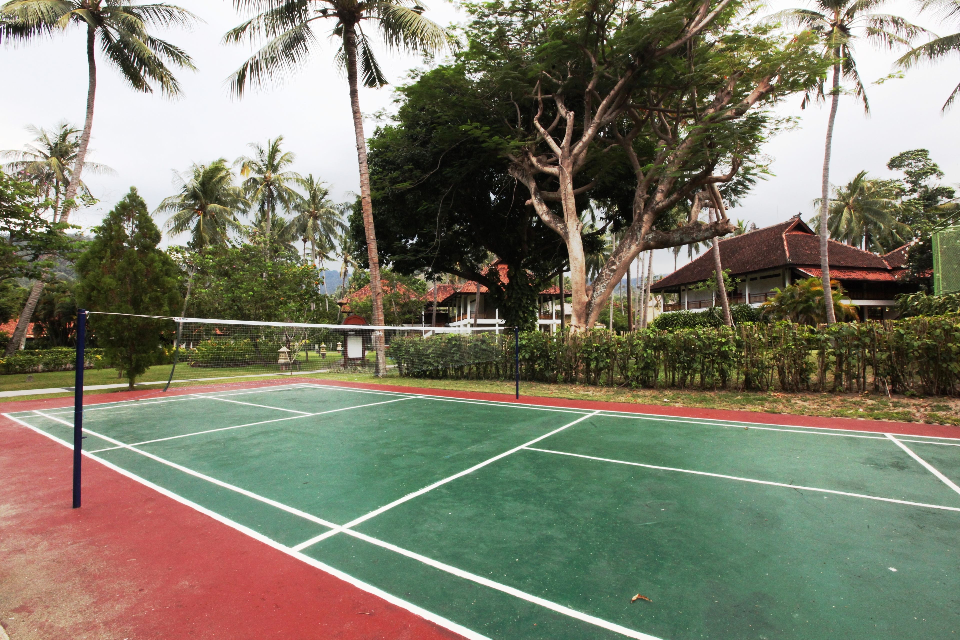 A tennis court with a net, surrounded by trees and a building in the background.