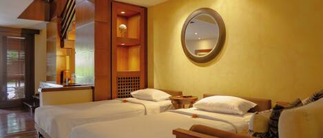 A hotel room with two beds, a wooden headboard, a round mirror, and a small table with a lamp.