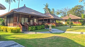 Un resort con edificios de techo de paja, un césped cuidado y palmeras.