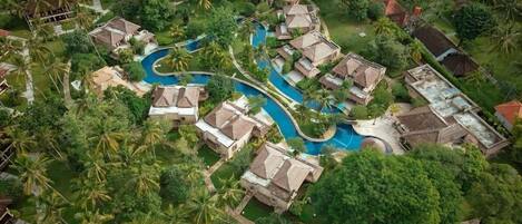 An aerial view of a resort with multiple bungalow-style accommodations, a central swimming pool, and lush greenery.