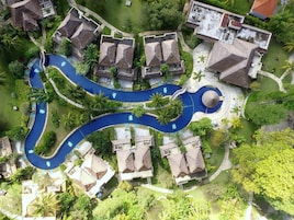 Vista aérea de un complejo turístico con una piscina sinuosa, edificios de techo de paja y exuberante vegetación.