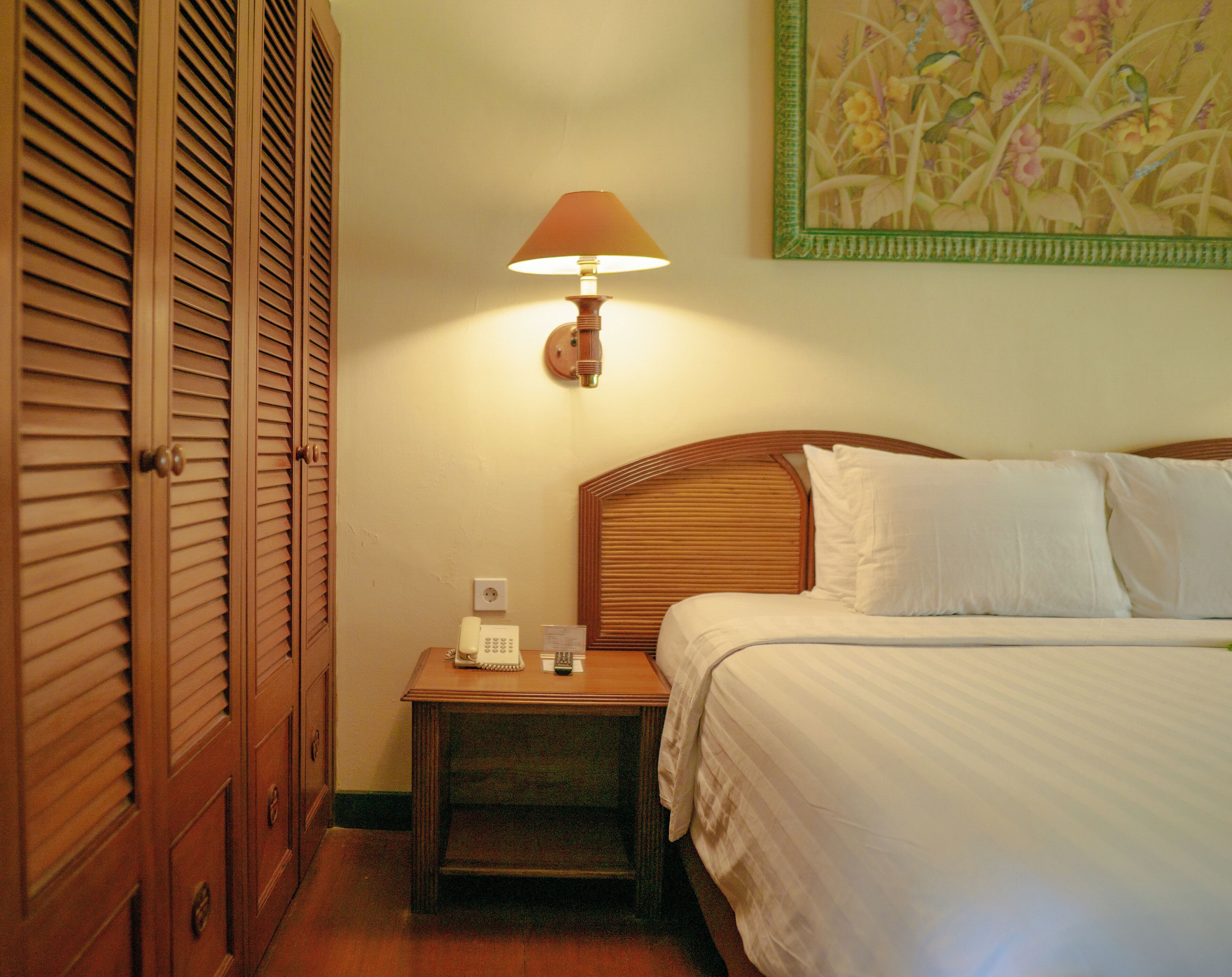 Habitación de hotel con cama, mesita de noche con lámpara, teléfono y luz empotrada en la pared.