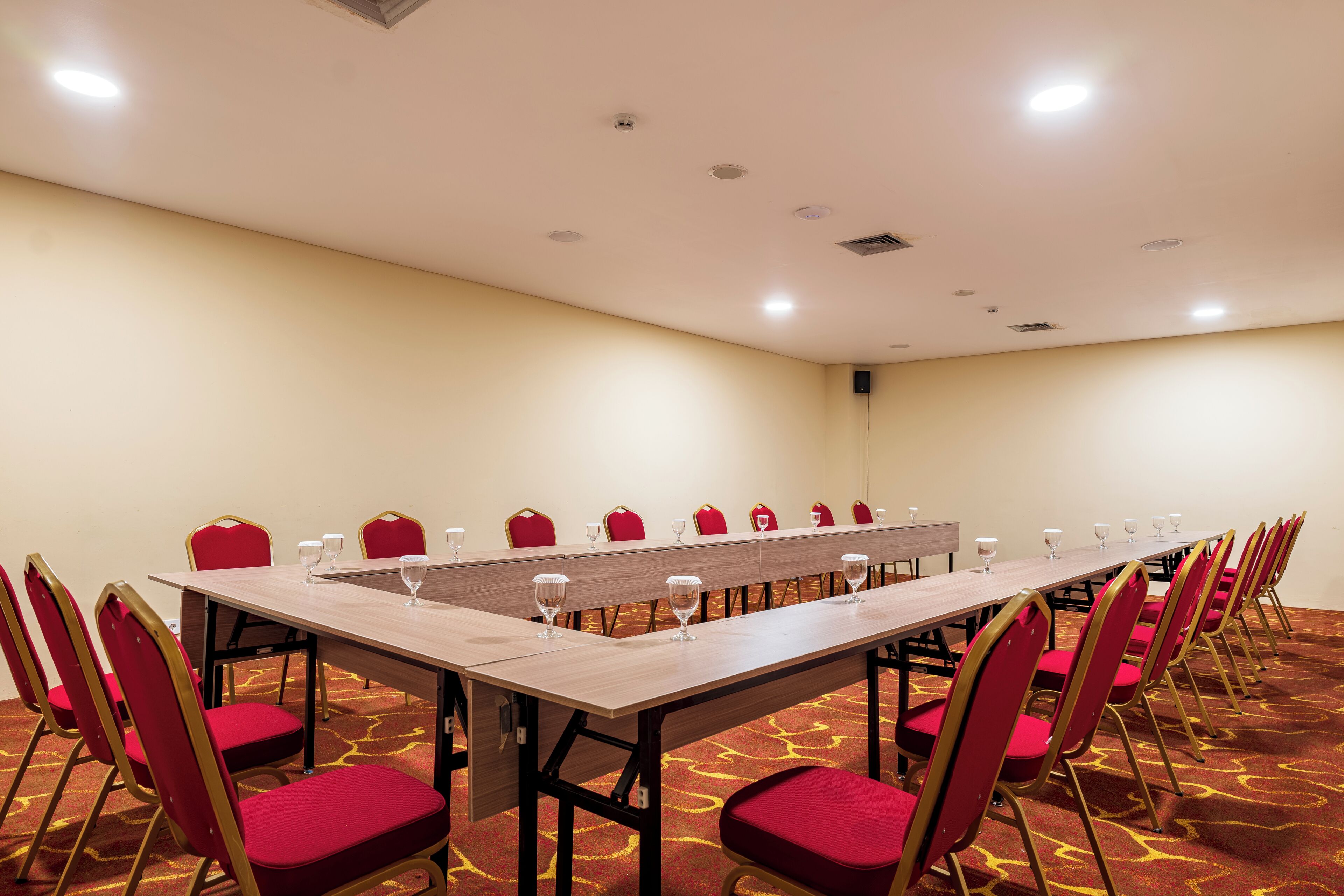 Una sala de conferencias con una mesa larga, sillas rojas y suelo alfombrado.