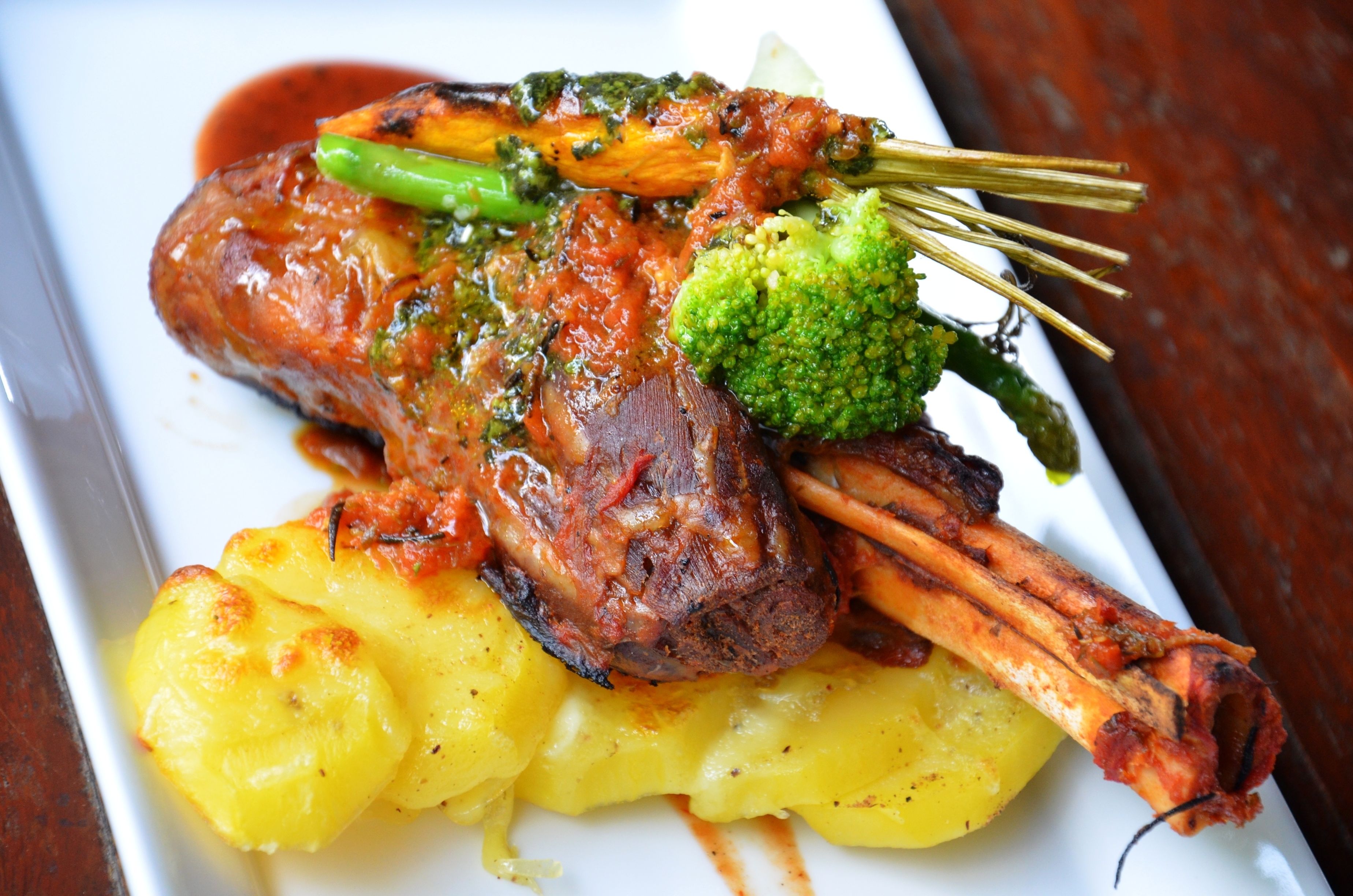 A plate of food with a lamb shank, broccoli, and potatoes.