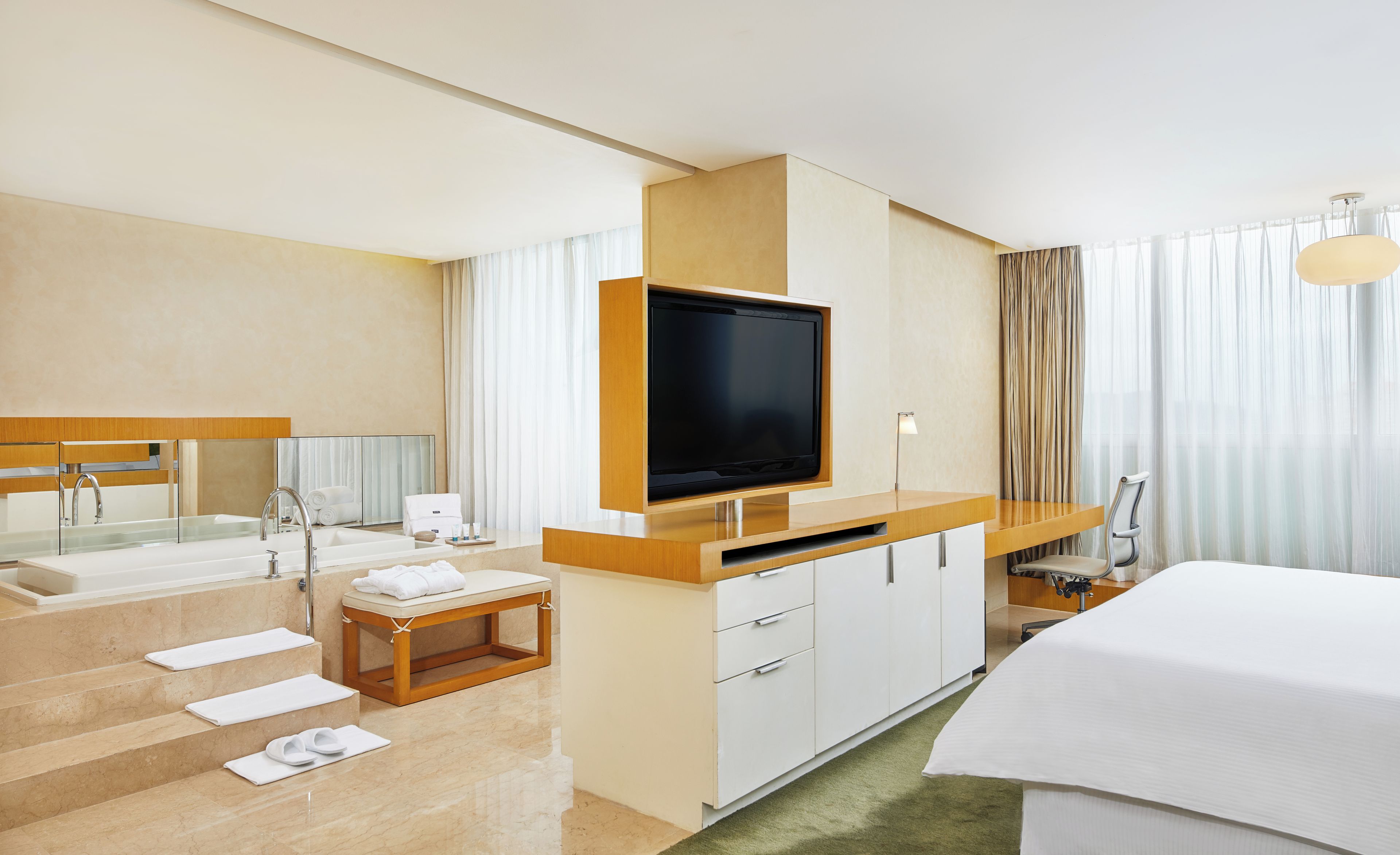 Habitación de hotel con televisión, escritorio, silla, cama, baño con lavamanos y espejo, y una escalera.
