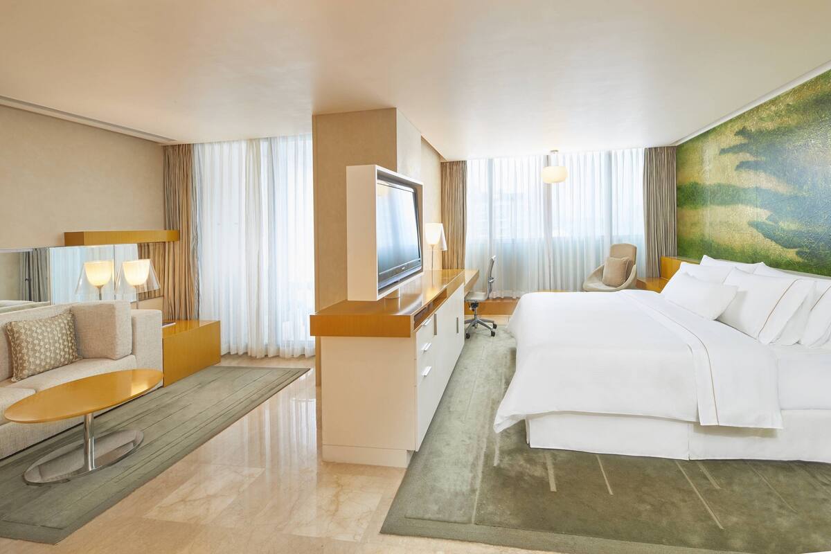 A hotel room with a bed, a desk, a chair, a sofa, and a TV.