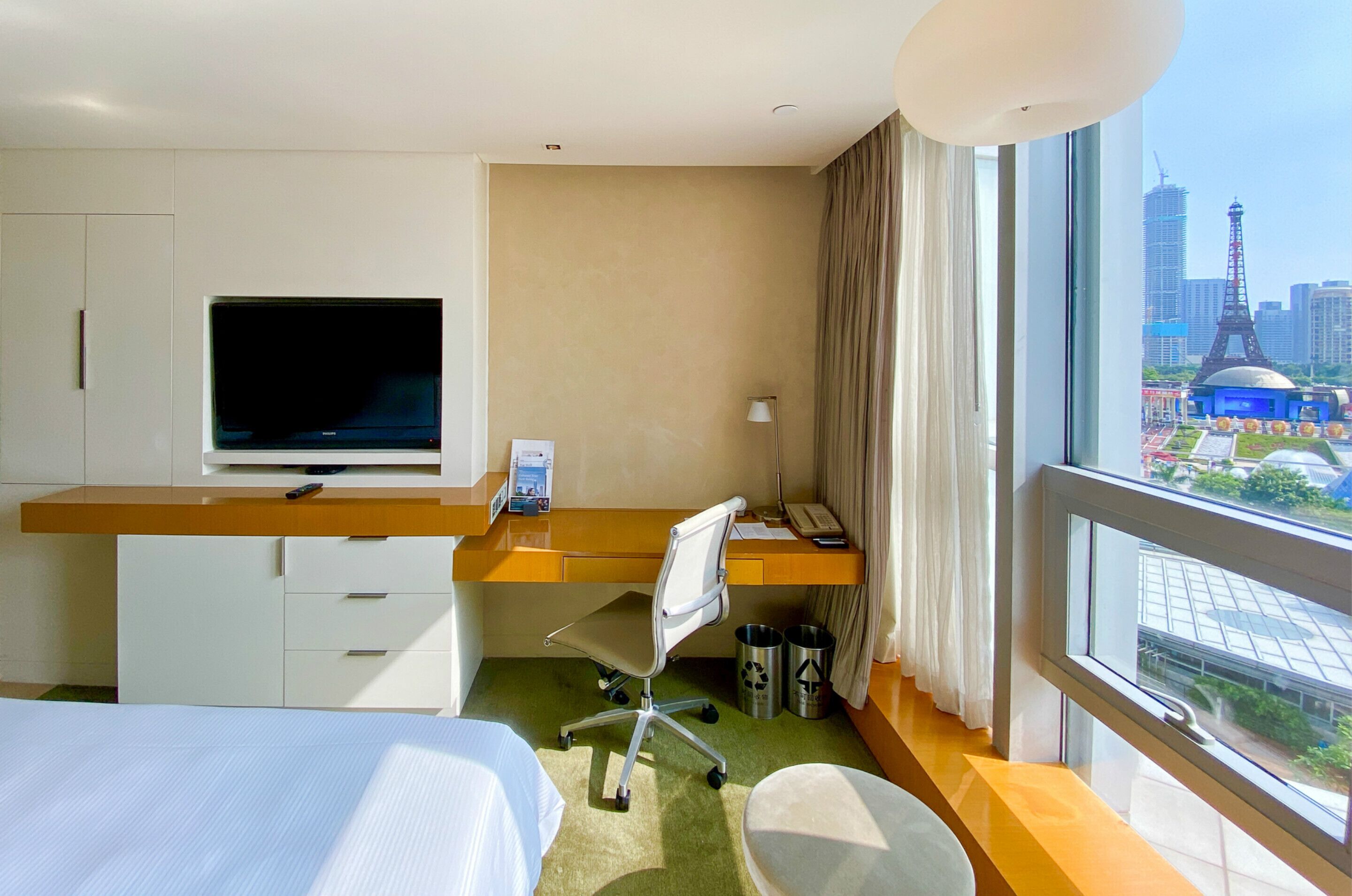 A hotel room with a bed, desk, chair, TV, and a window with a city view.