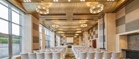 A conference room with rows of white chairs, large windows, and a patterned carpet.